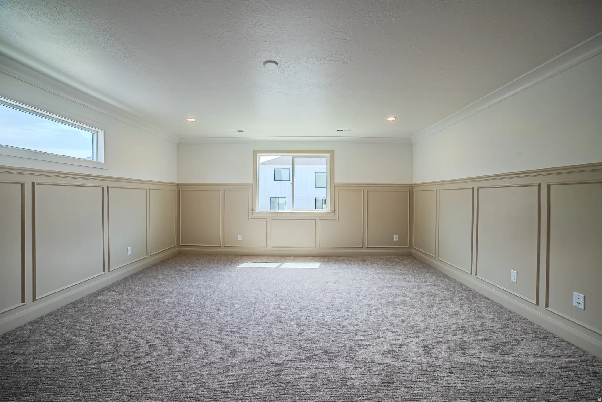 Spacious room featuring paneled wainscoting, crown molding, gray carpet, recessed lighting, and ample natural light from two windows