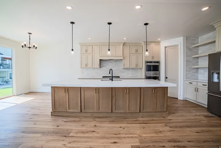 Spacious kitchen featuring a large island with under-counter storage, light-toned cabinetry, built-in double ovens, and wood-finish flooring