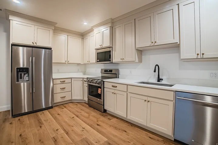 Kitchen featuring wood-finish flooring, light-toned cabinetry, stainless steel appliances, white countertops, and a matte black faucet