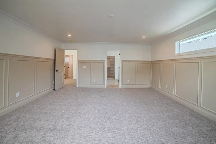 Spacious room featuring neutral carpeting, wainscoting paneling, crown molding, a transom window, and recessed lighting