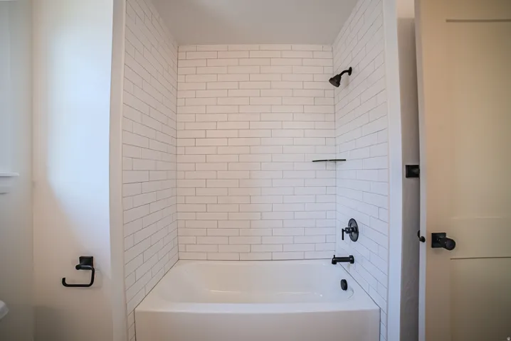 Bathtub and shower combination featuring white subway tile surround, matte black fixtures, and an integrated shelf