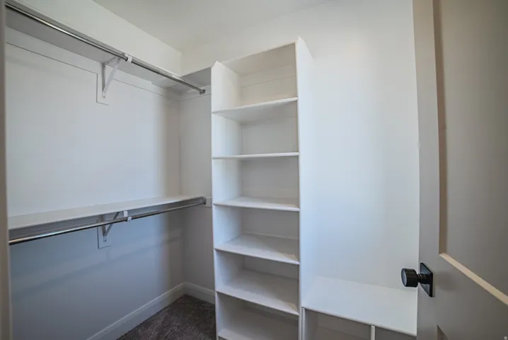 Walk-in closet featuring built-in shelving, two hanging rods, and a door with matte black hardware