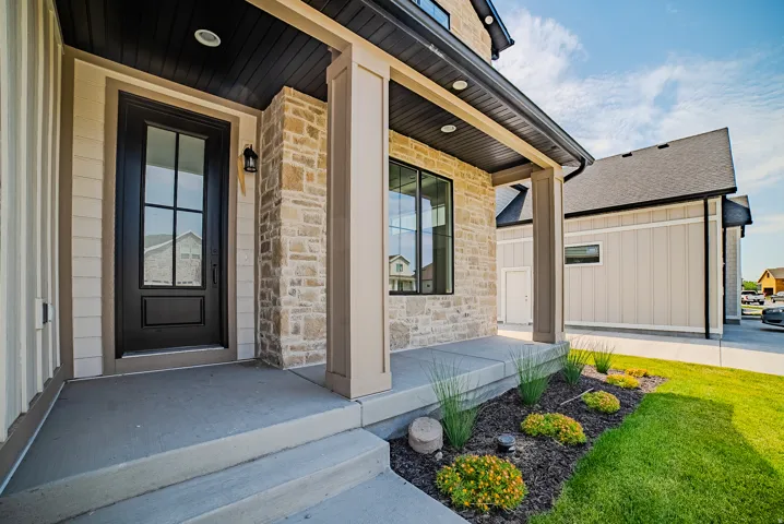 Inviting entryway featuring a dark-framed door with glass panels, textured stone cladding, and horizontal siding