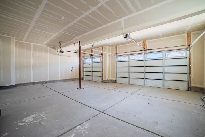 Two-bay garage with concrete flooring, two overhead doors featuring upper window panels, and exposed ceiling joists