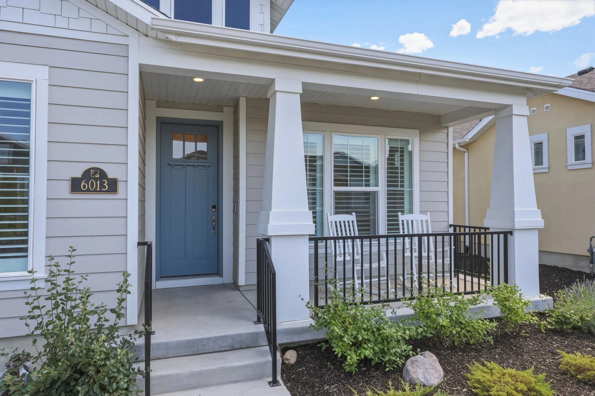 Covered front porch featuring a blue entry door with transom window, light gray siding, white trim, and dark metal railings