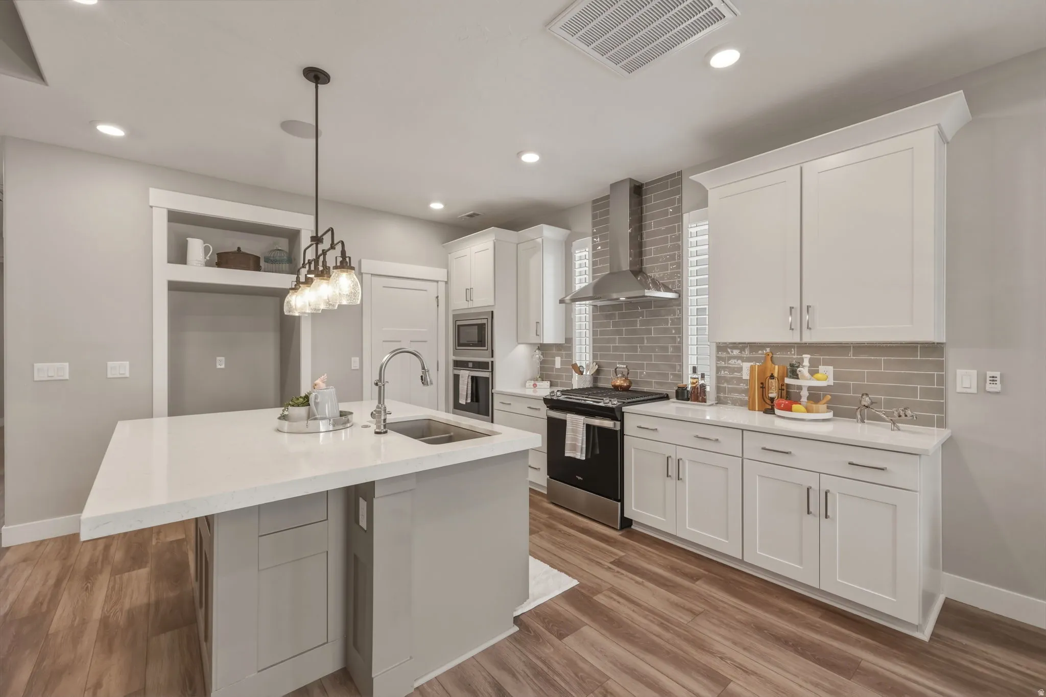 Spacious kitchen featuring an extra large island with quartz countertops, white cabinetry, tile backsplash, stainless steel appliances, and LVP flooring.