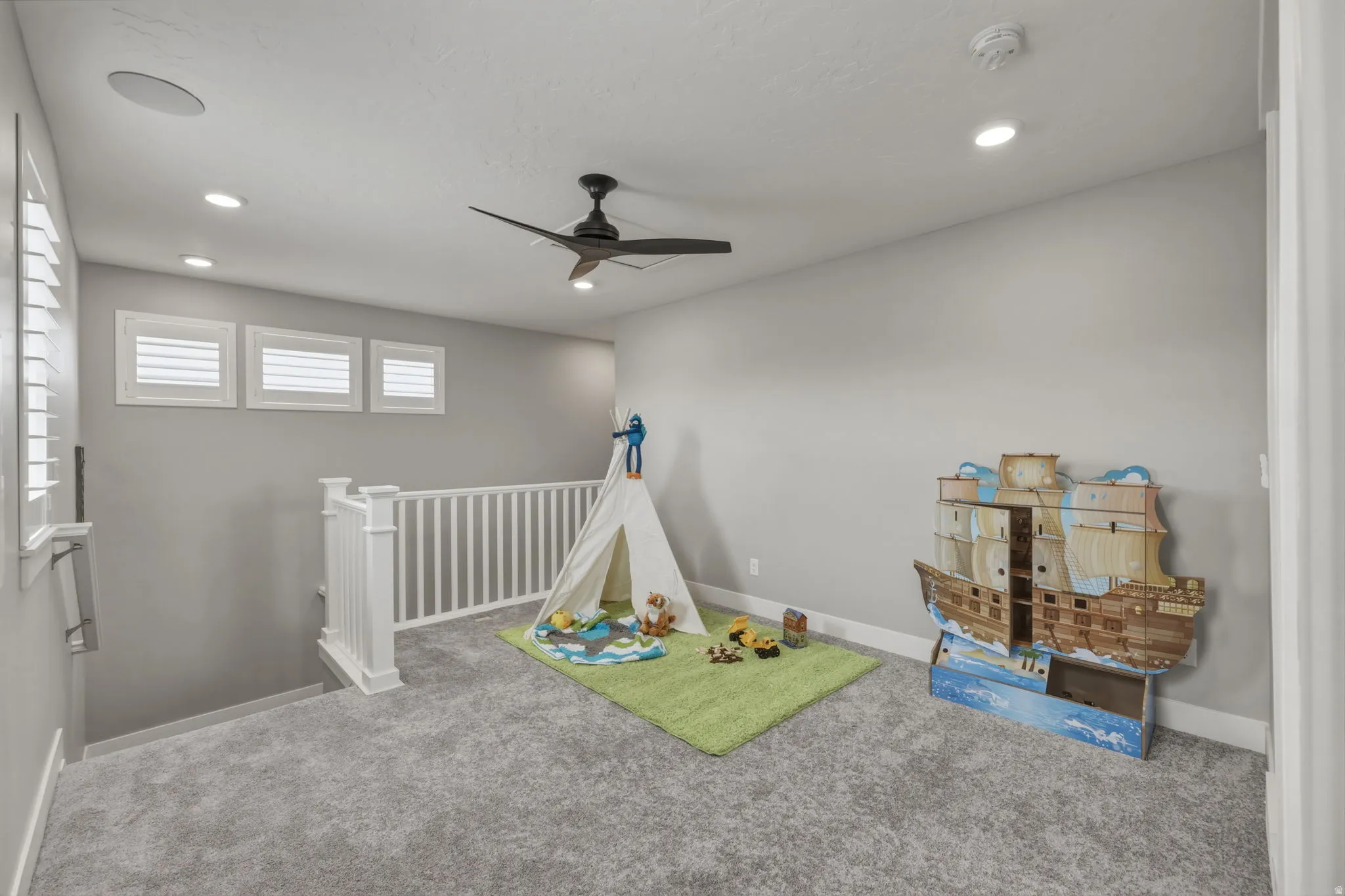 Carpeted loft area featuring a white balustrade railing, gray carpet flooring and a ceiling fan