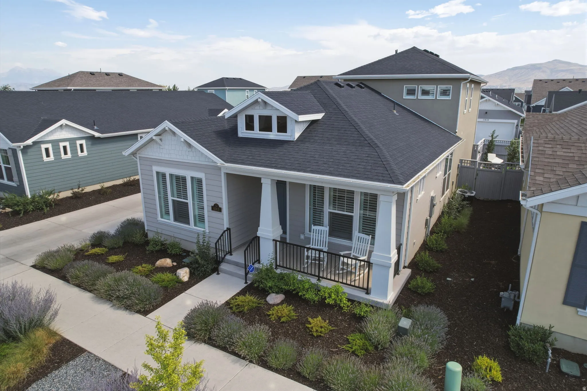 Contemporary cottage-style residence featuring a covered front porch with white columns, a dormer window, and a dark shingle roof
