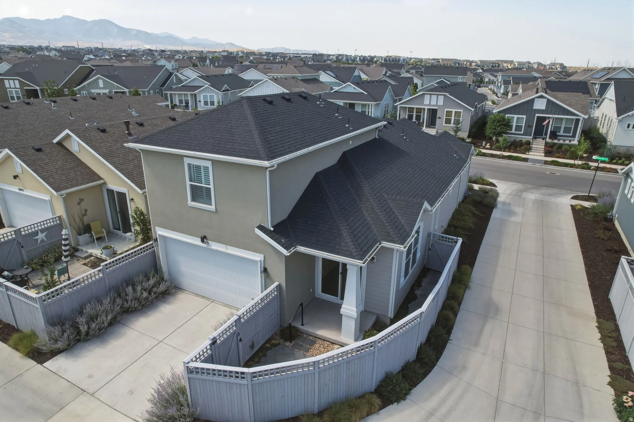 Contemporary stucco exterior with a dark shingle roof, featuring a two-car garage, fenced landscaping, and concrete paving