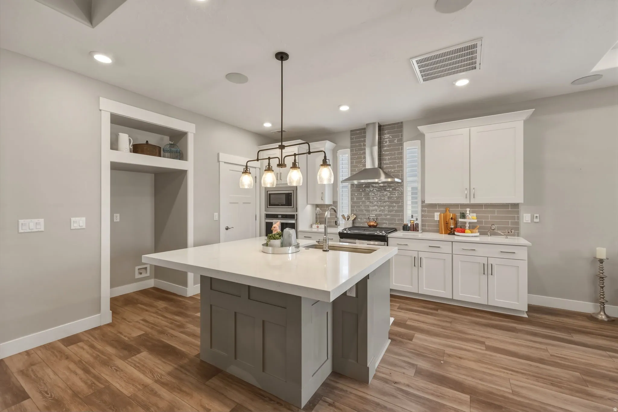 Spacious kitchen featuring an extra large island with quartz countertops, white cabinetry, tile backsplash, stainless steel appliances, and LVP flooring.