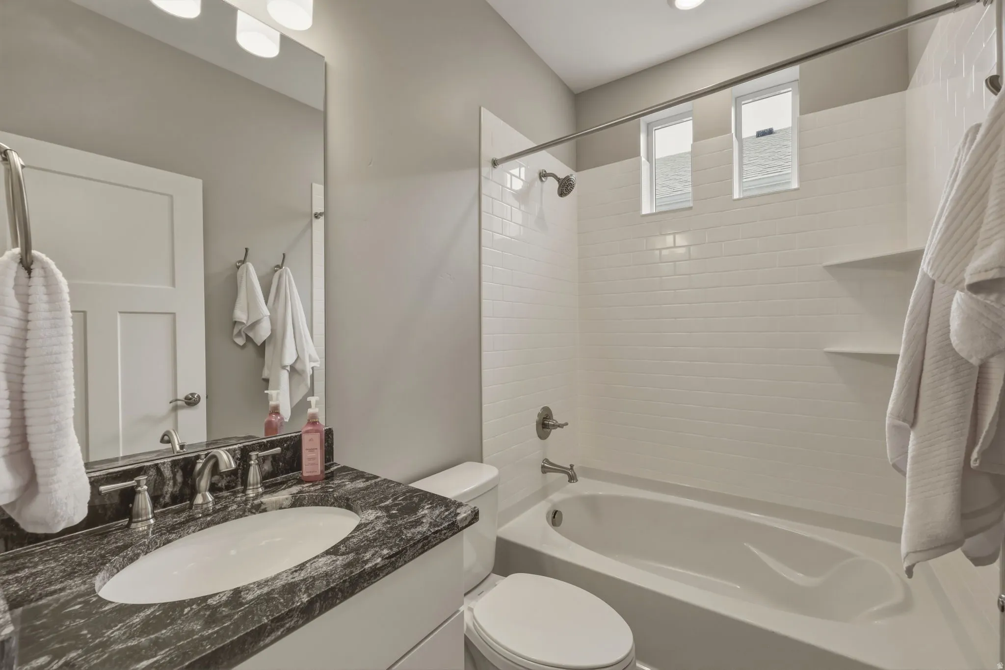 Full bathroom with granite countertops, vanity with an undermount sink, brushed nickel fixtures, a full-width mirror, a white subway tile shower surround with an integrated bathtub.
