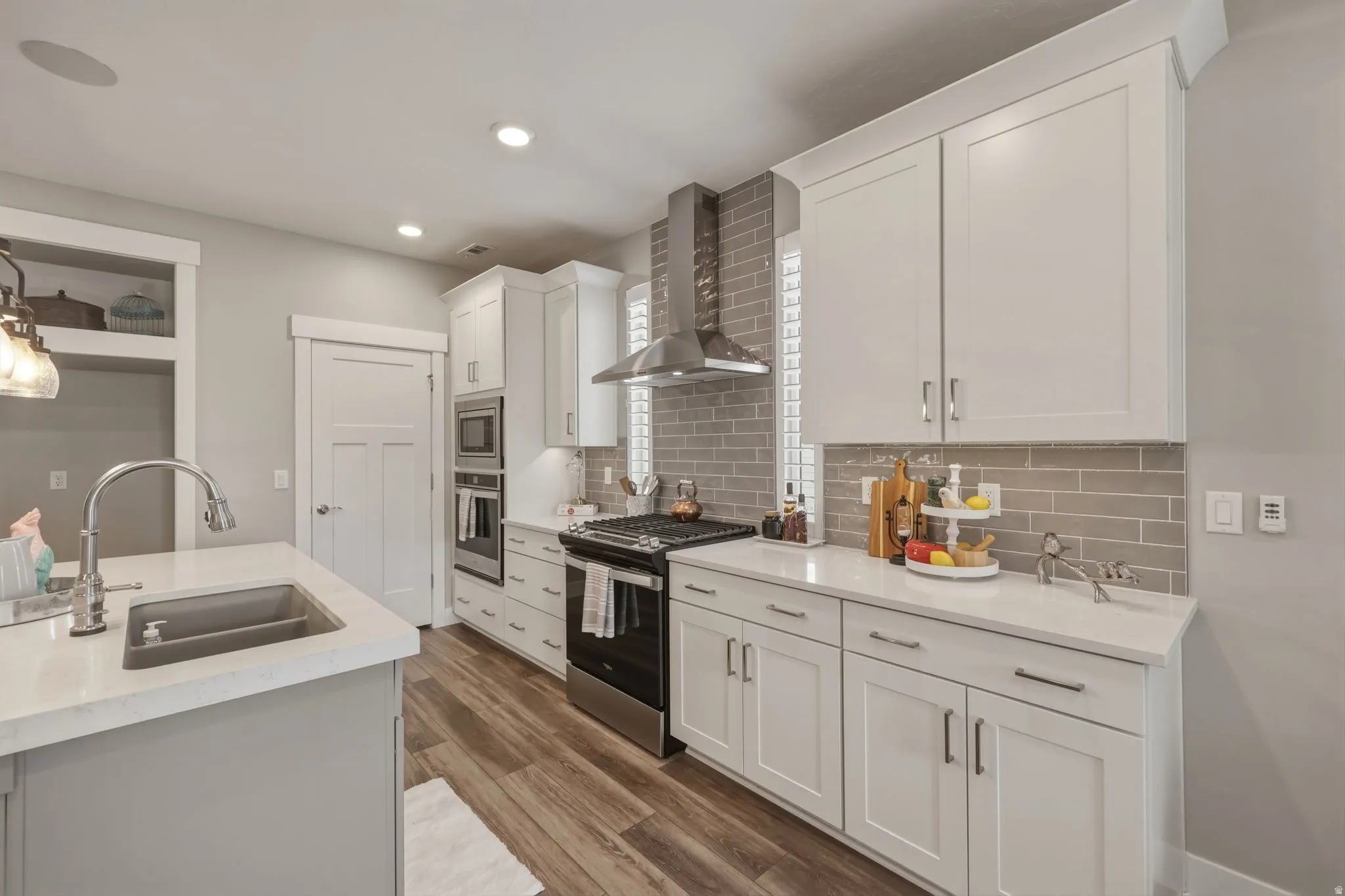 Spacious kitchen featuring an extra large island with quartz countertops, white cabinetry, tile backsplash, stainless steel appliances, and LVP flooring.
