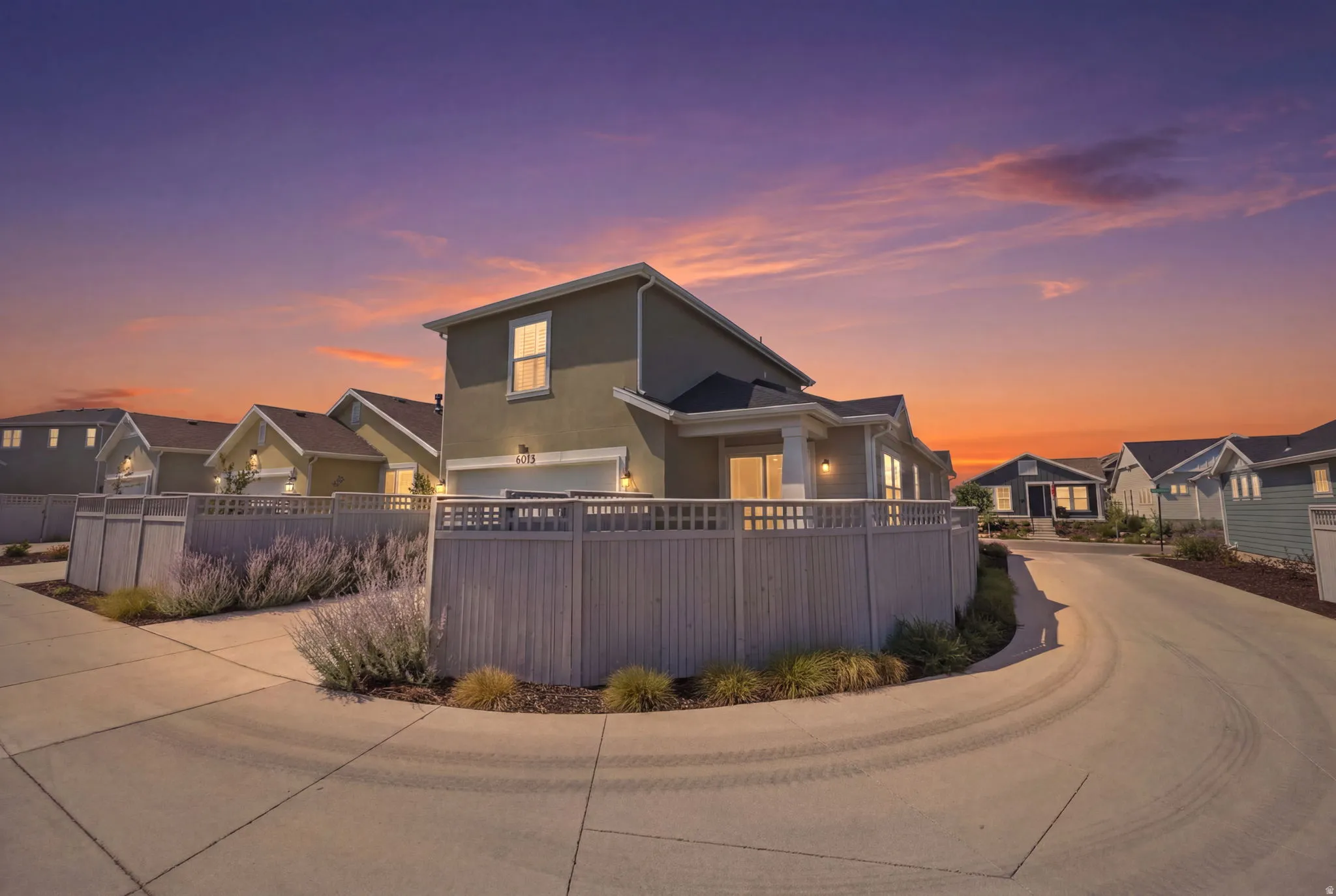 Contemporary stucco exterior with a dark shingle roof, featuring a two-car garage, fenced landscaping, and concrete paving