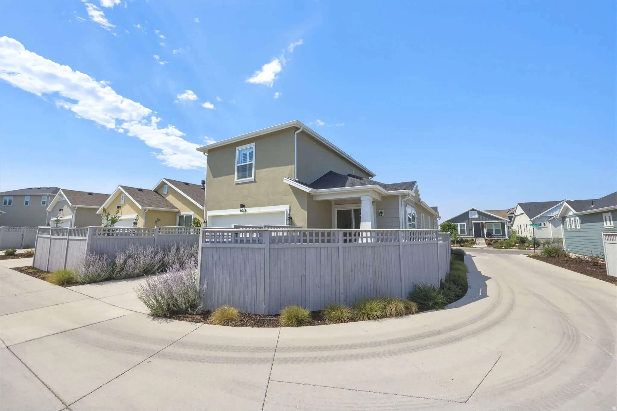 Contemporary stucco exterior with a dark shingle roof, featuring a two-car garage, fenced landscaping, and concrete paving