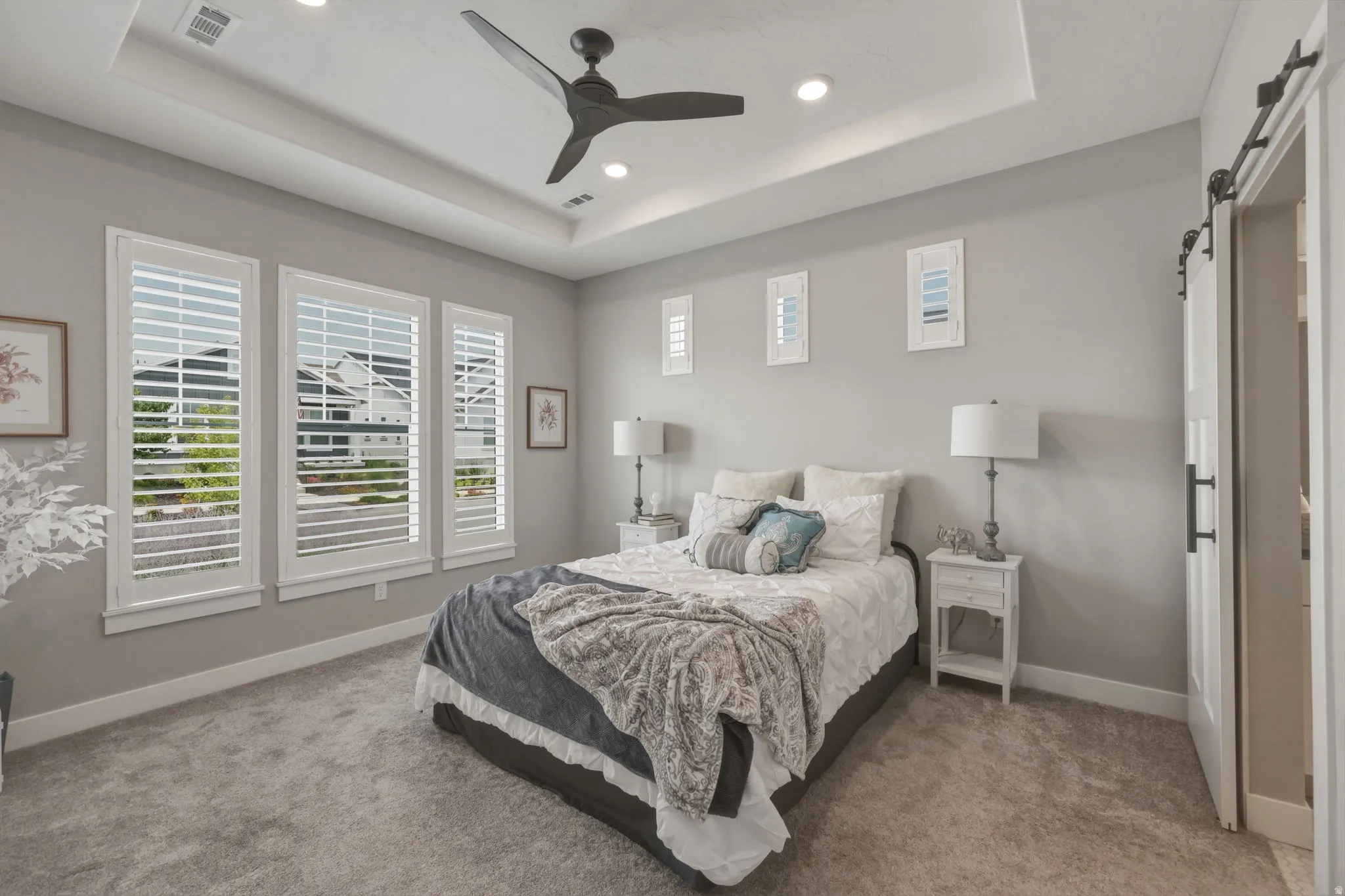 Sunlit primary bedroom with carpeting, recessed lighting and ceiling fan.