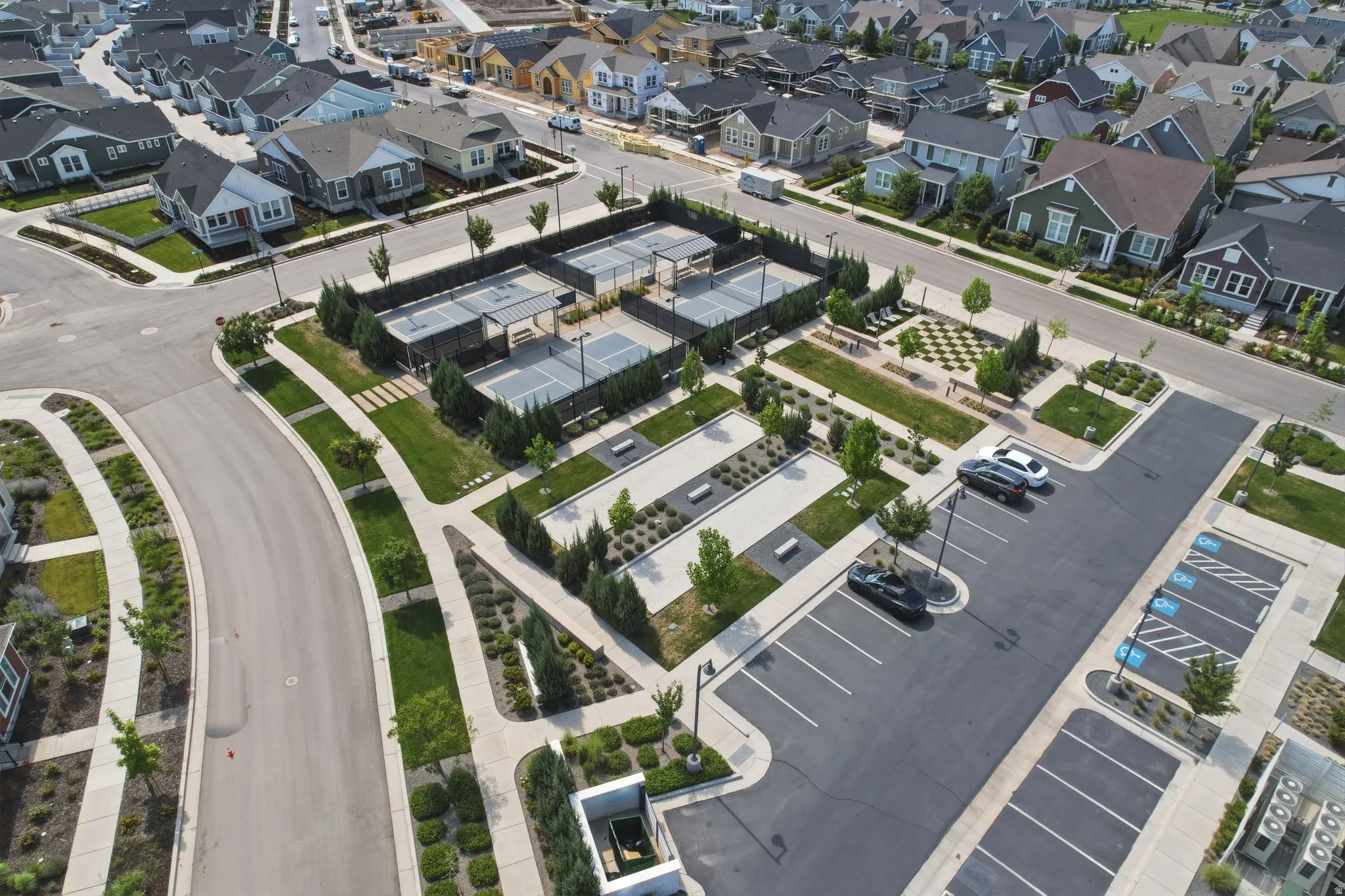 Community amenities featuring multiple tennis courts, a surface parking lot, paved walkways, and landscaped green spaces with mature trees and shrubbery