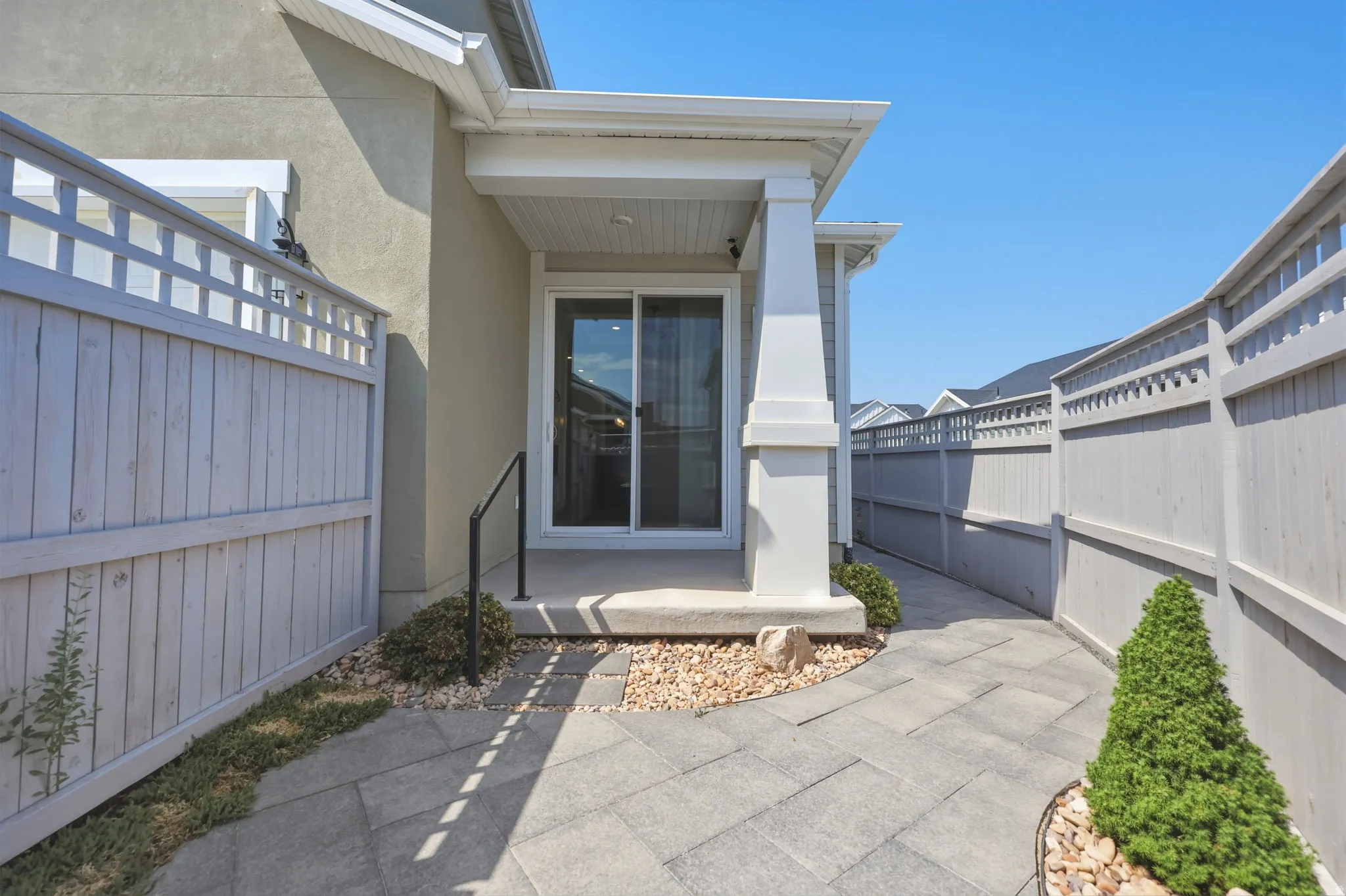 Covered patio with a sliding glass door entry, surrounded by a privacy fence and paver walkway