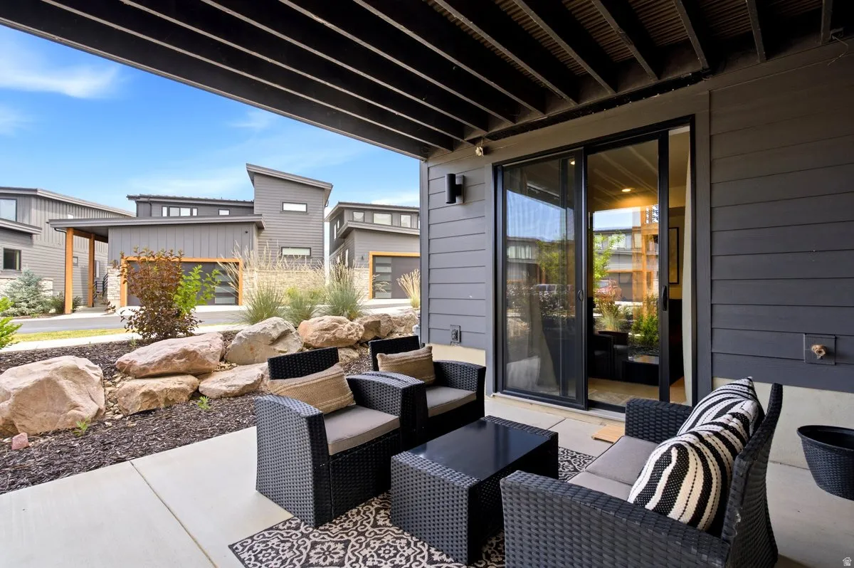 Covered concrete patio featuring modern gray siding, black framed sliding glass door, and integrated outdoor lighting