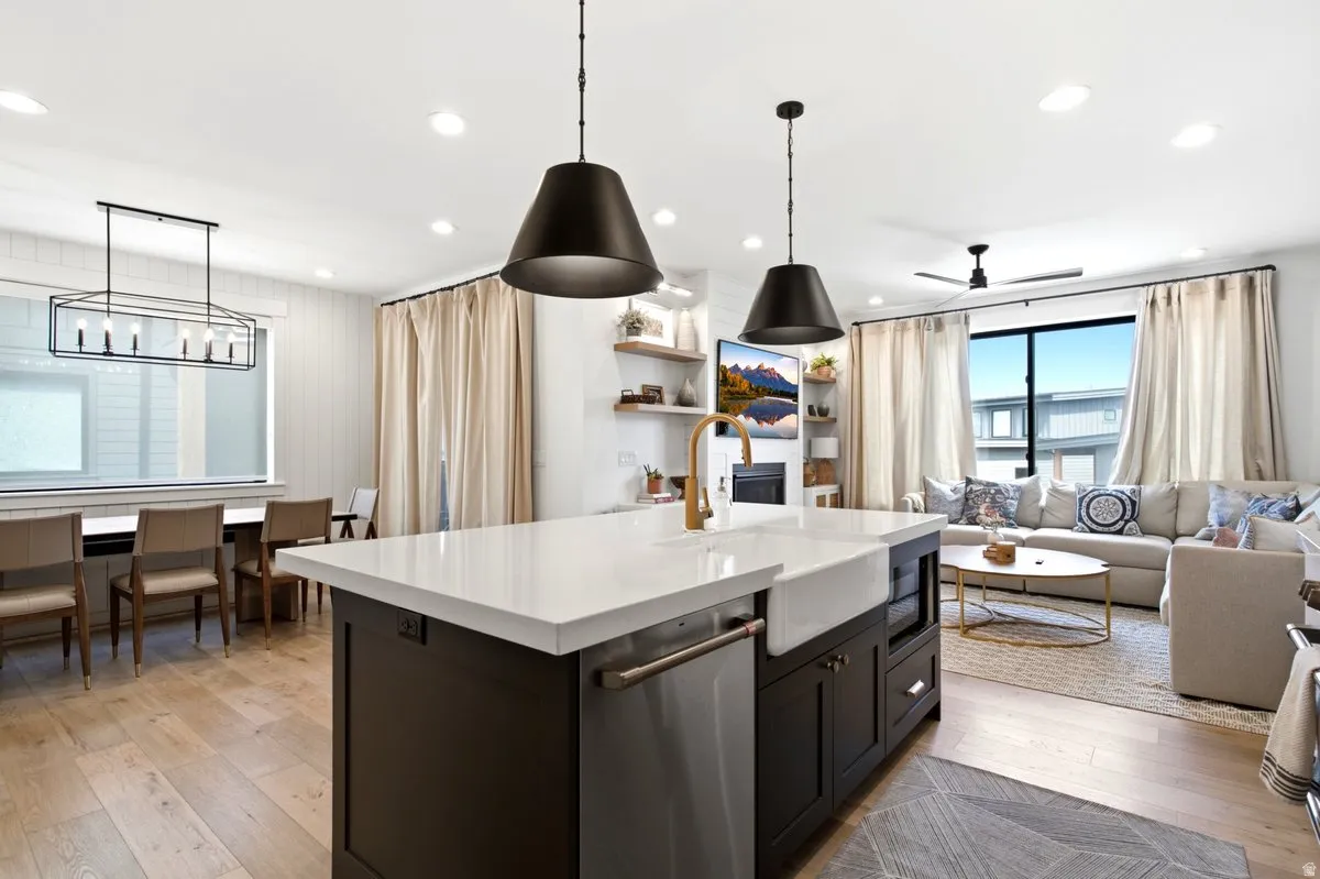 Open-concept living space featuring a central island with a white countertop and farmhouse sink, wood-finish flooring, recessed lighting, and a dining area with a linear chandelier