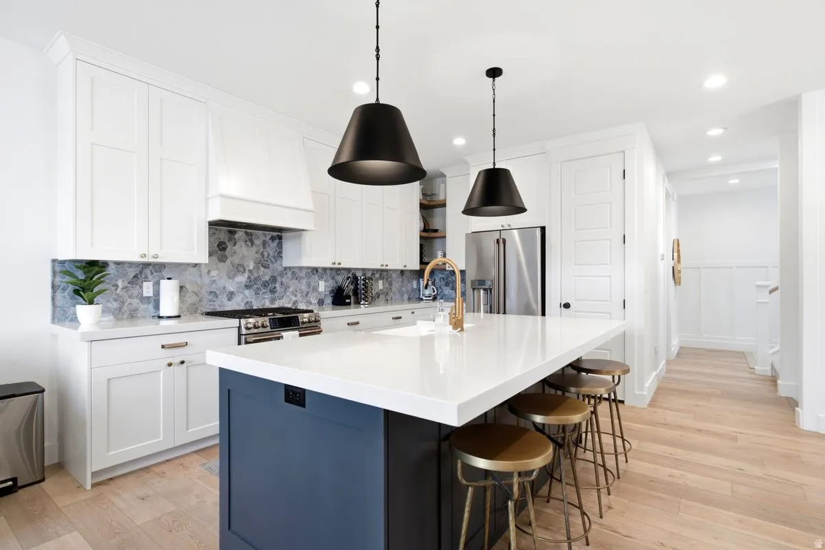 Kitchen featuring white shaker cabinetry, an expansive center island with a white countertop, a tile backsplash, stainless steel appliances, and wood-finish flooring