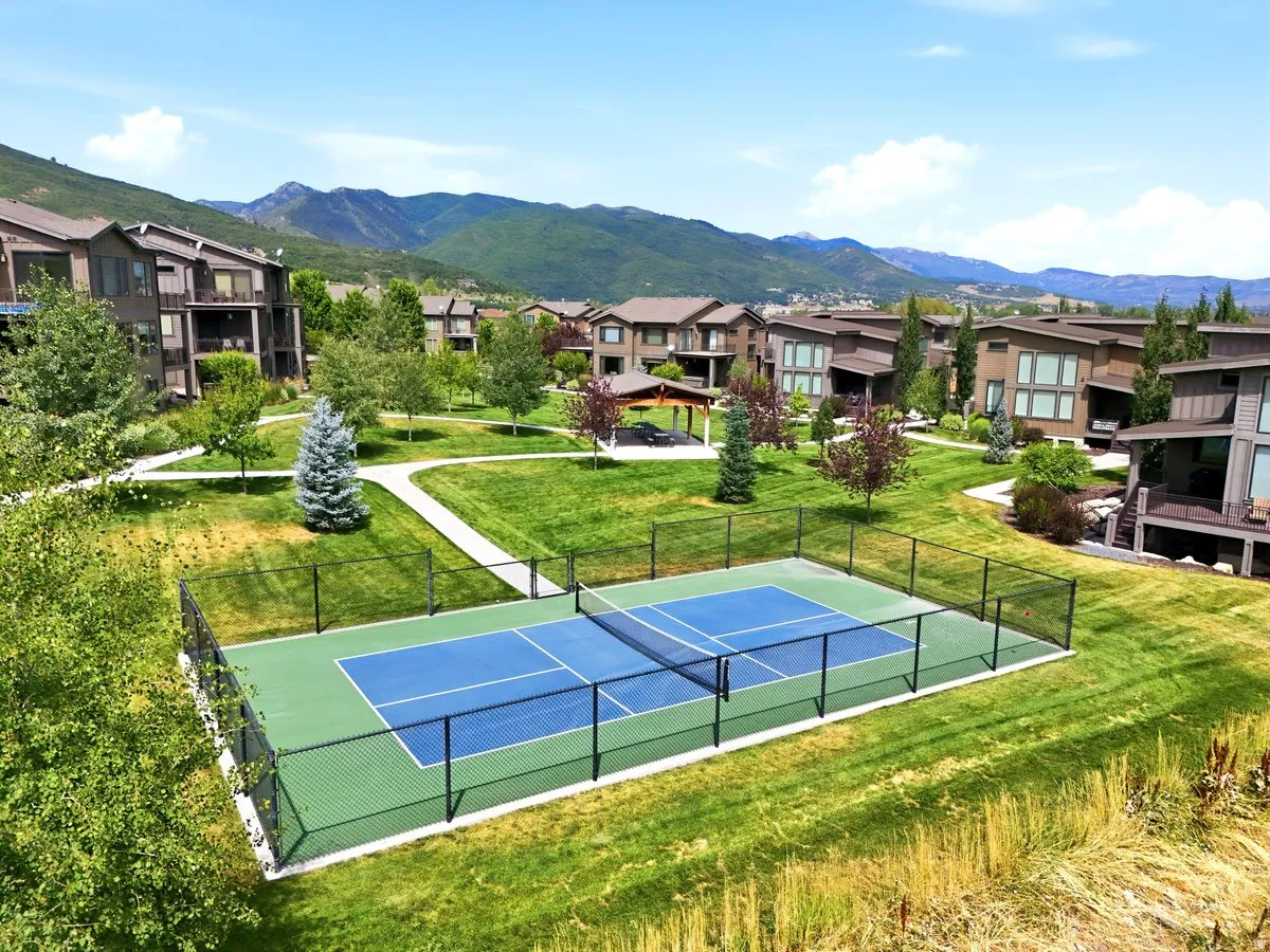 Fenced pickleball court with blue and green surfacing, surrounded by manicured lawns and mature trees