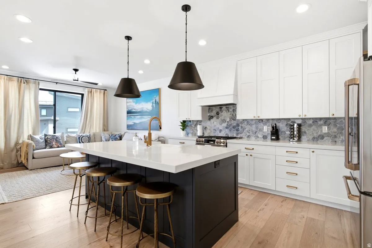Kitchen featuring a large central island with seating, white shaker cabinetry, patterned tile backsplash, and light wood-finish flooring