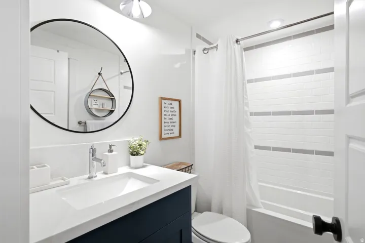 Contemporary bathroom featuring a dark blue vanity, integrated sink with chrome faucet, and a large circular mirror
