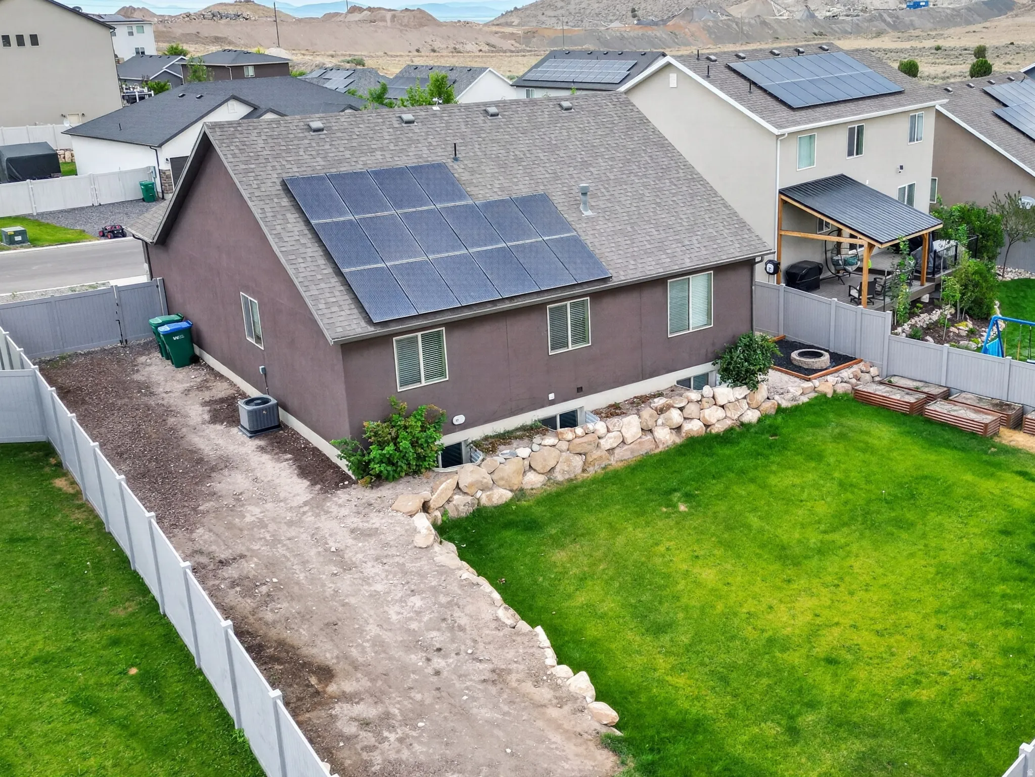 Expansive fenced backyard featuring a manicured lawn, raised garden beds, and rock landscaping