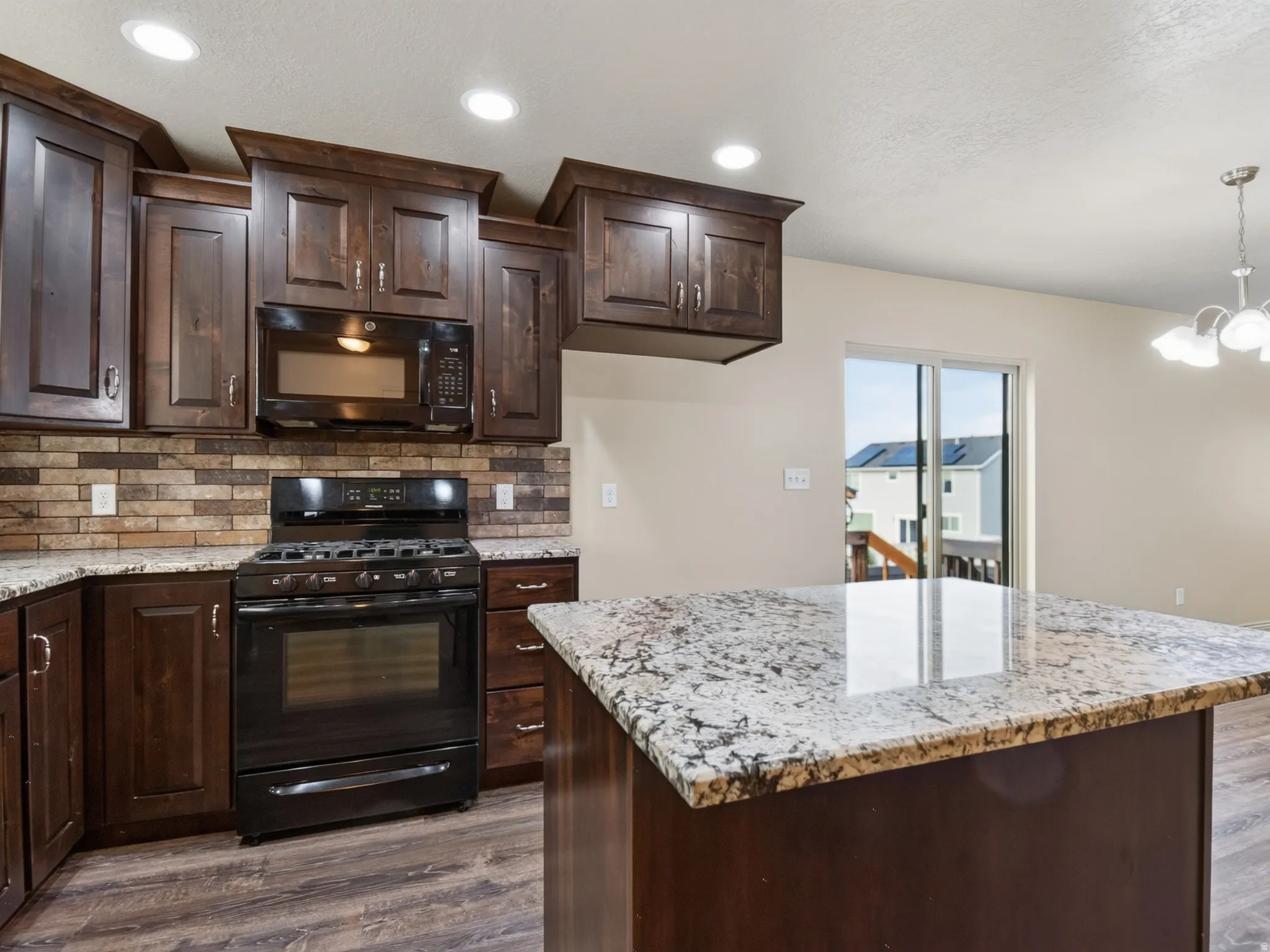 Kitchen featuring dark wood cabinetry, granite countertops, a tiled backsplash, and wood-finish flooring