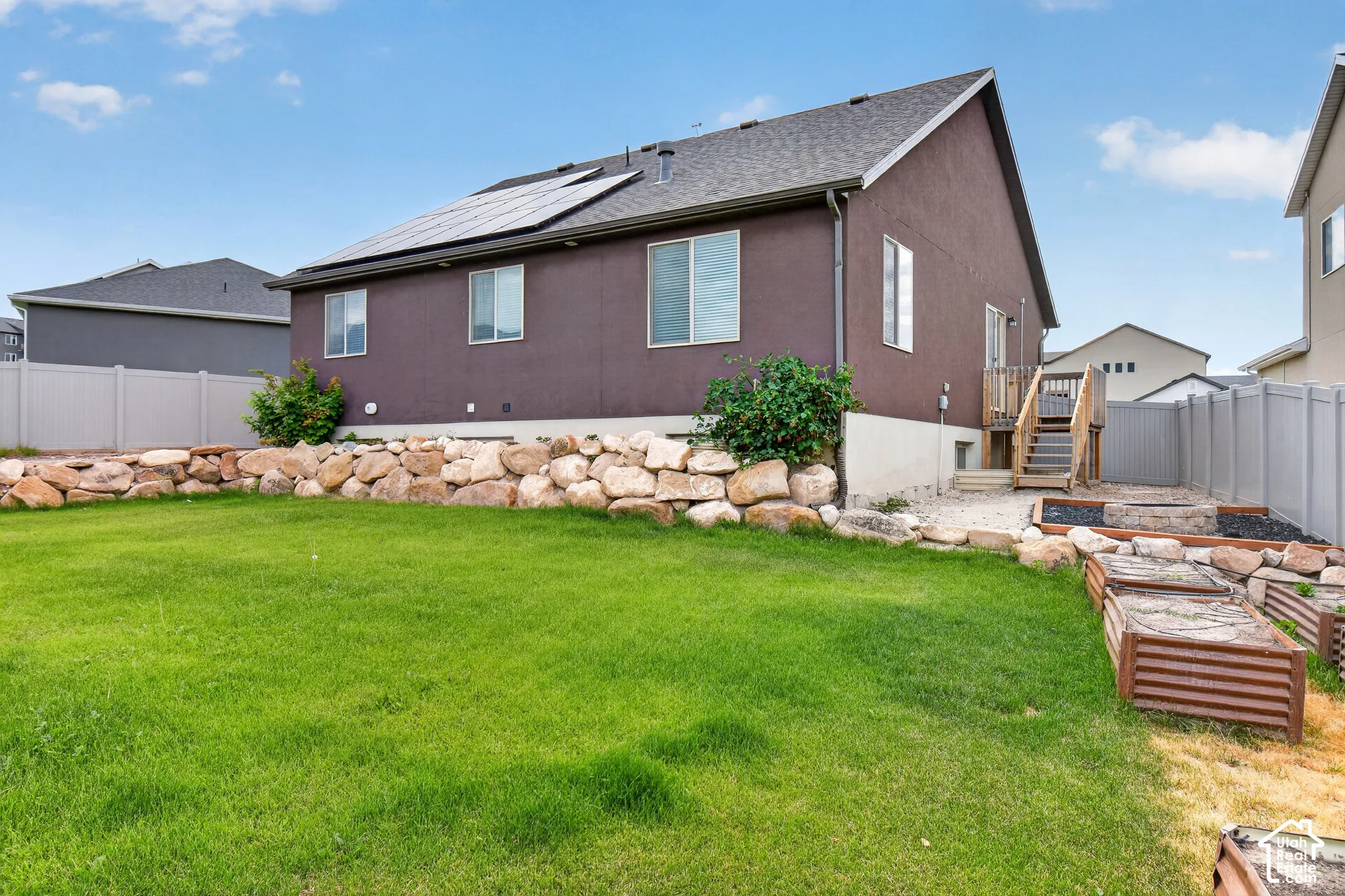 Expansive backyard featuring a green lawn, rock retaining wall, and raised garden beds