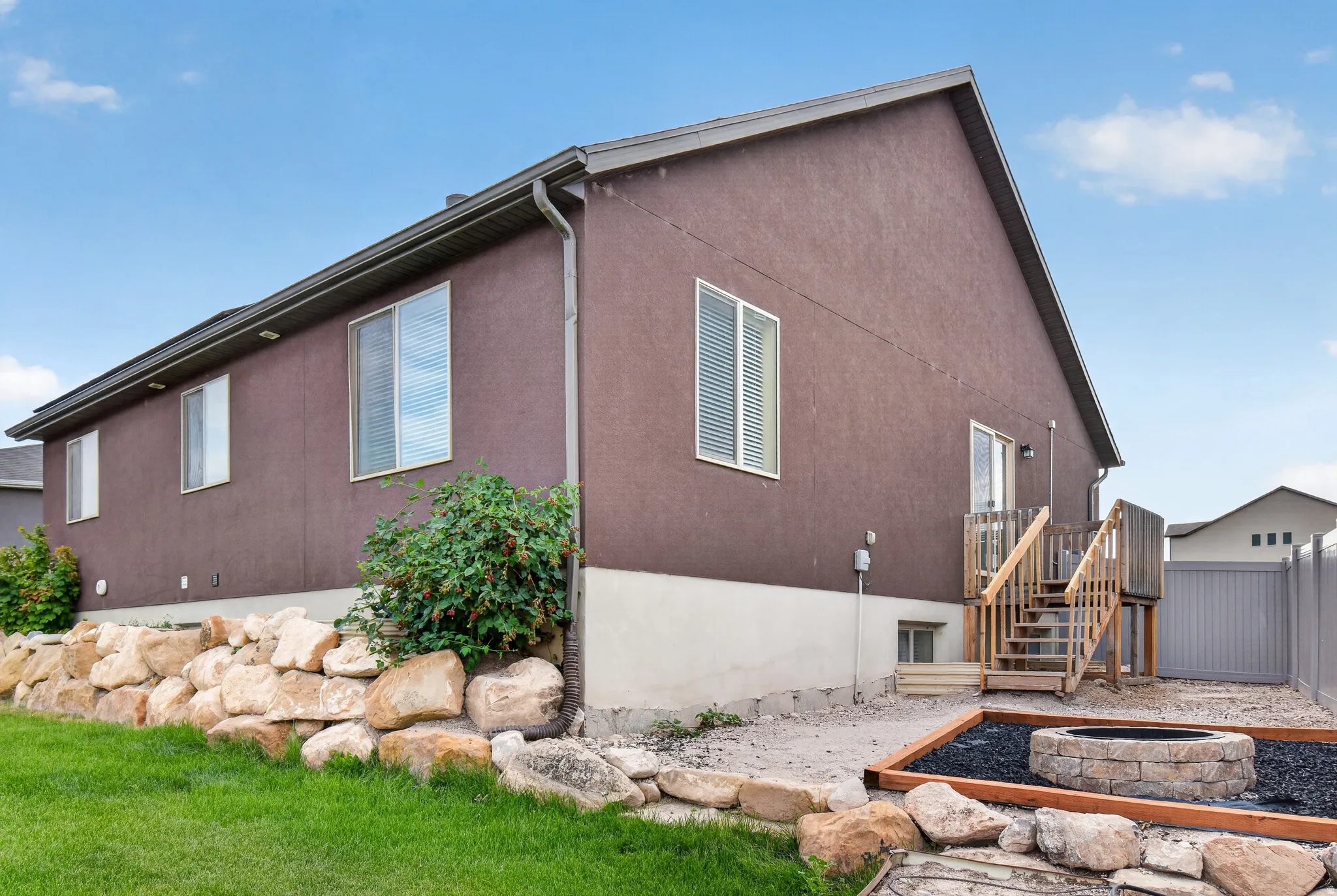 Rear exterior featuring brown stucco siding, a wooden deck with stairs, and a built-in stone fire pit