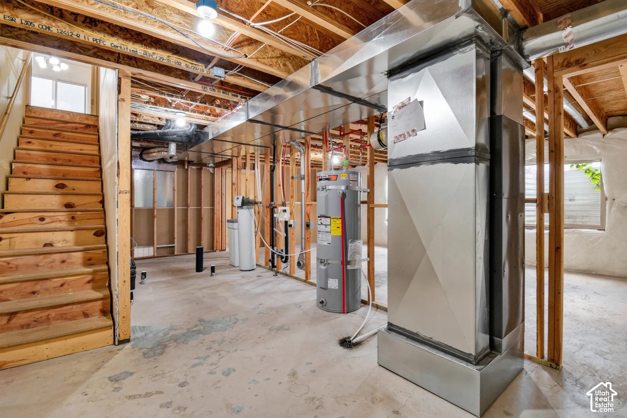 Unfinished basement featuring exposed wood framing, concrete flooring, and an exposed utility area with water heater and water softener systems