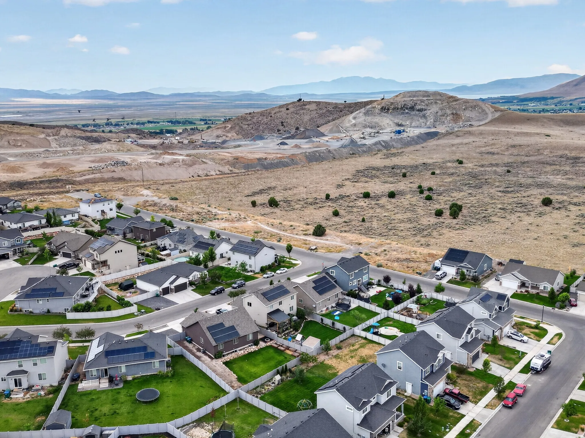 Aerial perspective of a suburban neighborhood featuring residential homes, paved streets, and a backdrop of distant mountains and a valley