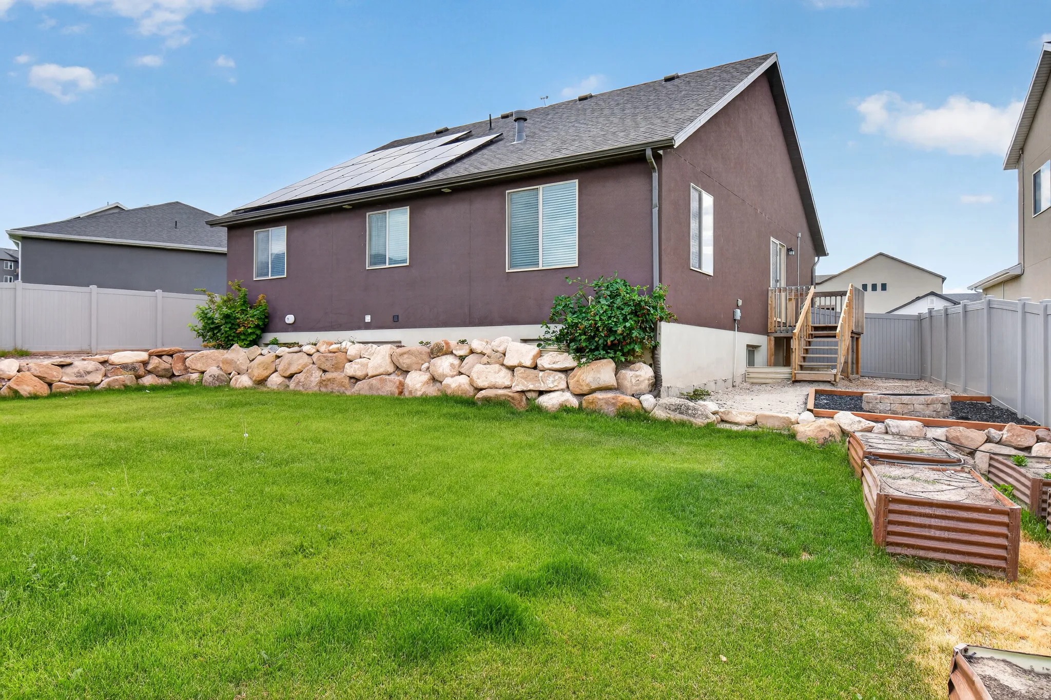 Expansive backyard featuring a green lawn, rock retaining wall, and raised garden beds