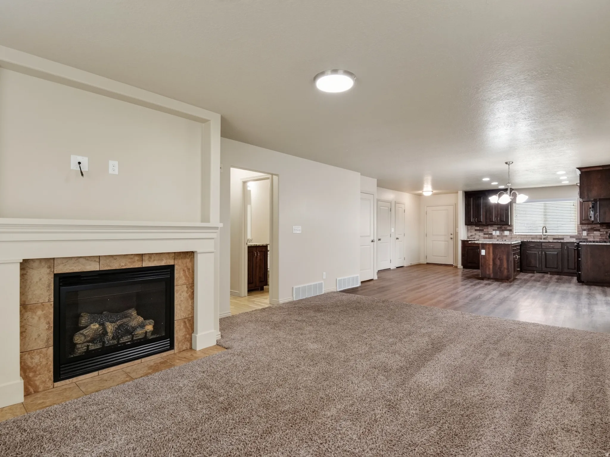 Living area featuring a gas fireplace with a tiled surround and white mantel, an integrated wall recess, and plush carpeting