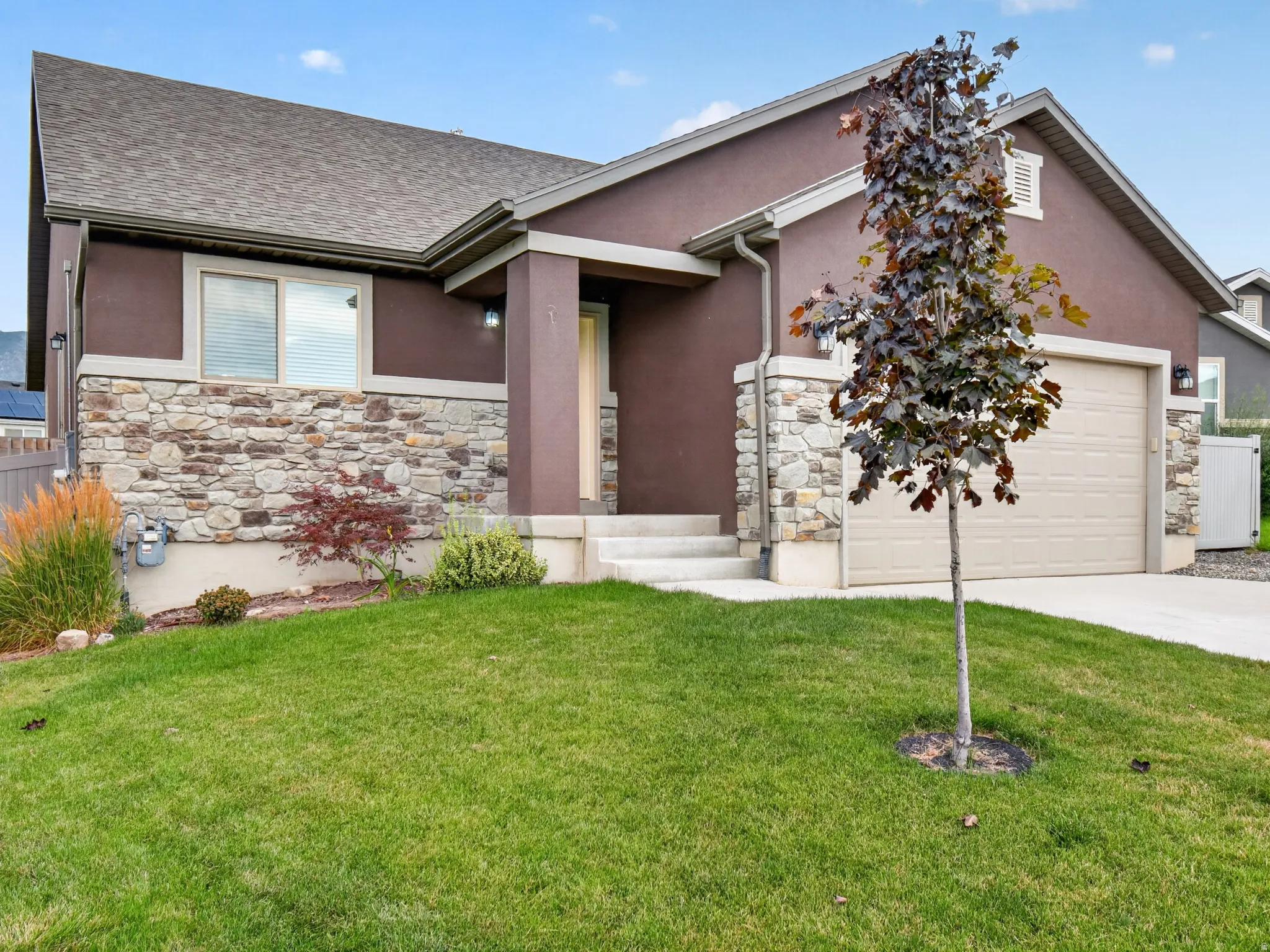 Stucco and stone exterior featuring an attached garage, covered entryway, and a low-sloped roofline