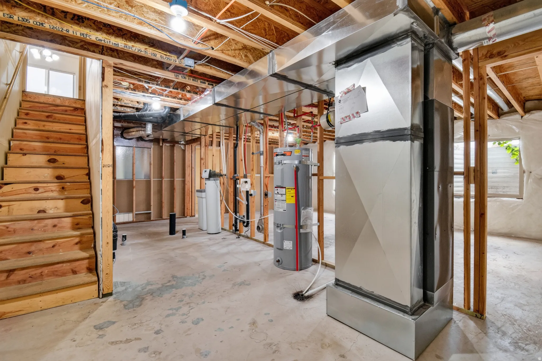 Unfinished basement featuring exposed wood framing, concrete flooring, and an exposed utility area with water heater and water softener systems