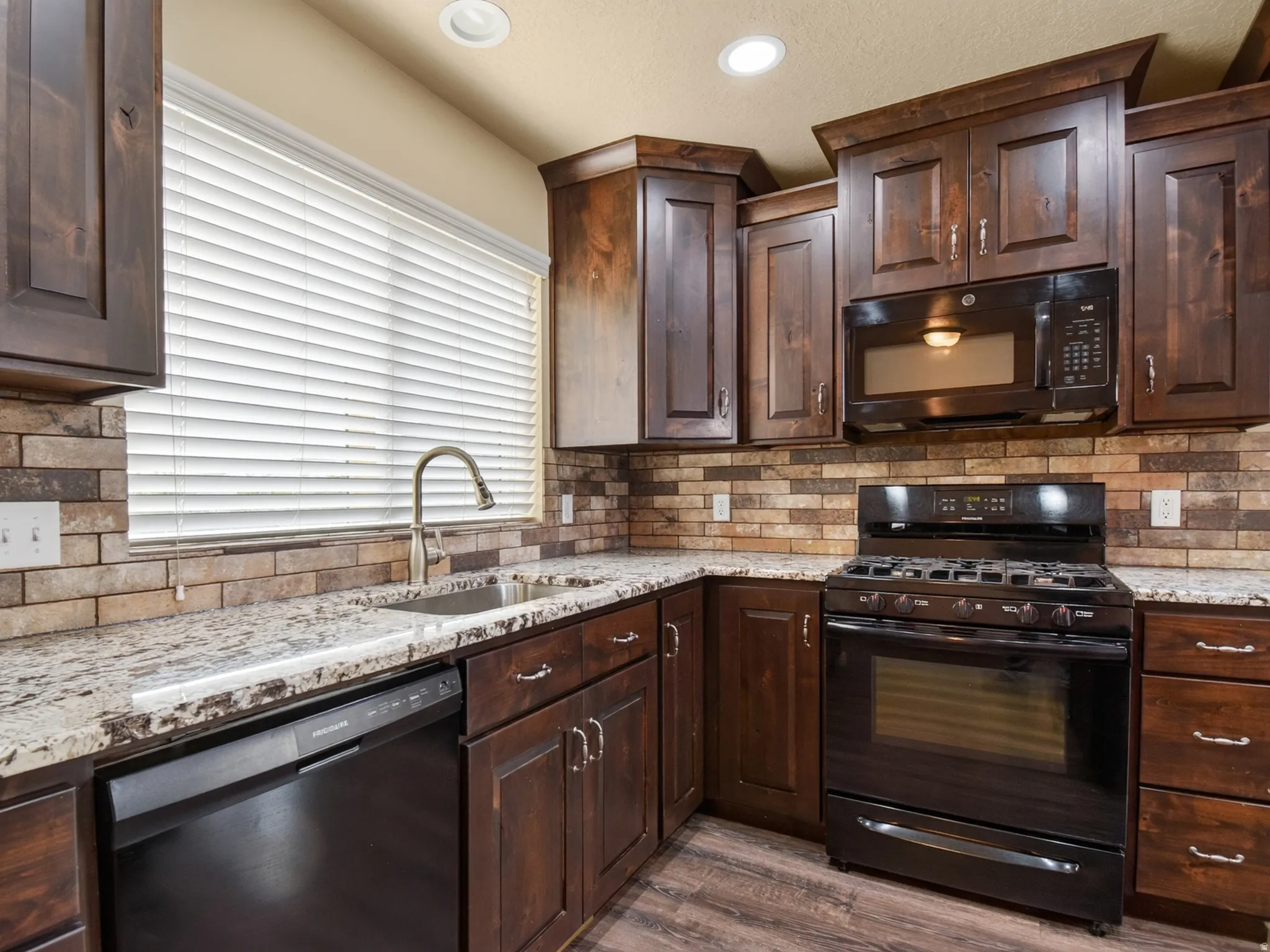 Kitchen featuring wood-finish cabinetry, light-toned granite countertops, and a full tile backsplash