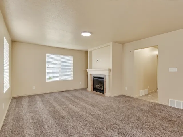 Living area featuring a fireplace with a white mantel, neutral carpeting, and two windows with horizontal blinds