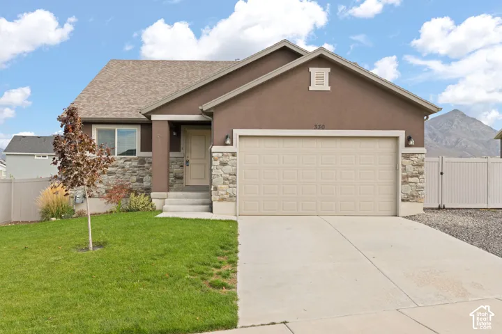 Single-story exterior featuring a stone veneer facade, stucco siding, a concrete driveway, a two-car garage, and mountain scenery