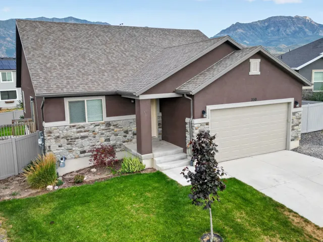 Contemporary residential exterior featuring a stone and stucco facade, a two-car garage, and a peaked roofline