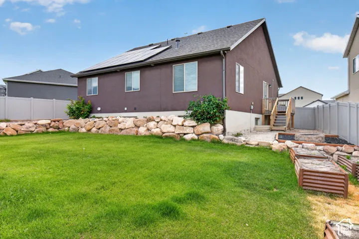 Expansive backyard featuring a green lawn, rock retaining wall, and raised garden beds