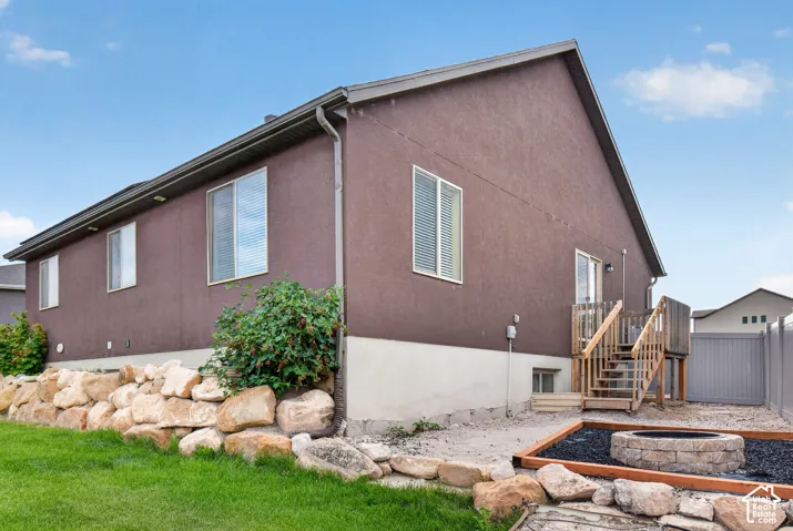 Rear exterior featuring brown stucco siding, a wooden deck with stairs, and a built-in stone fire pit