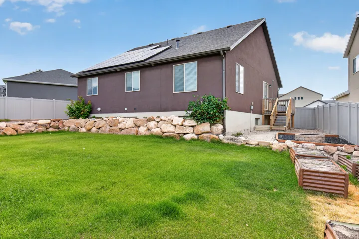 Expansive backyard featuring a green lawn, rock retaining wall, and raised garden beds