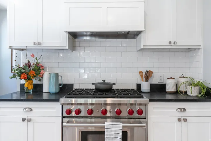 Contemporary kitchen featuring a stainless steel range with red accent knobs, white shaker cabinetry, and dark countertops