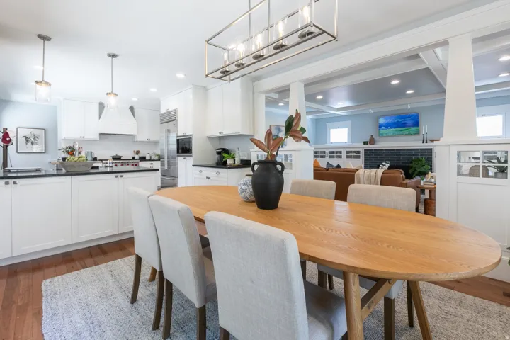 Open-concept dining area with wood-finish flooring, a contemporary linear chandelier, and decorative columns