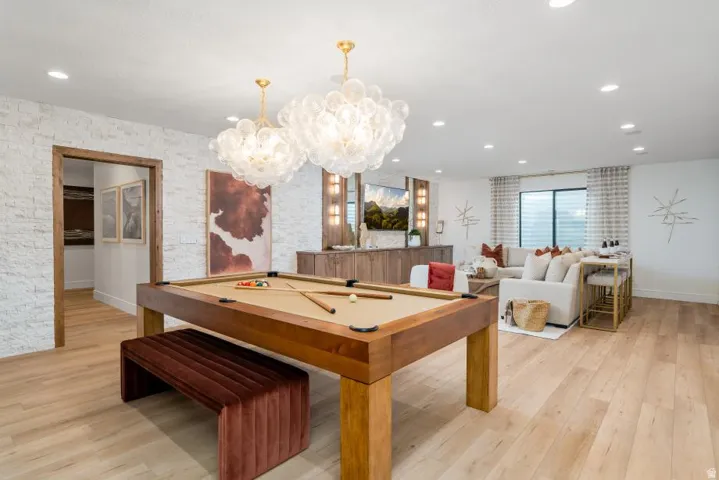 Recreation room showcasing a wood-finish pool table with coordinating bench seating, elegant crystal pendant lighting, wide-plank wood-finish flooring, and abundant natural light from expansive windows