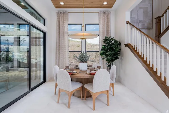 Spacious dining area featuring a wood-panel ceiling, large sliding glass doors, white tile flooring, and an open staircase with wood and white railings