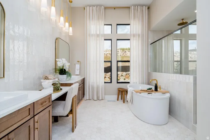 Bathroom featuring a freestanding soaking tub, large format tiled shower with glass enclosure, dual vanities with integrated sinks, and hexagon tile flooring
