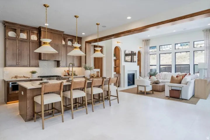 Open-concept kitchen and living area featuring custom wood cabinetry with glass-front upper cabinets, stainless steel appliances, white quartz countertops, pendant lighting, and wood-finish flooring throughout